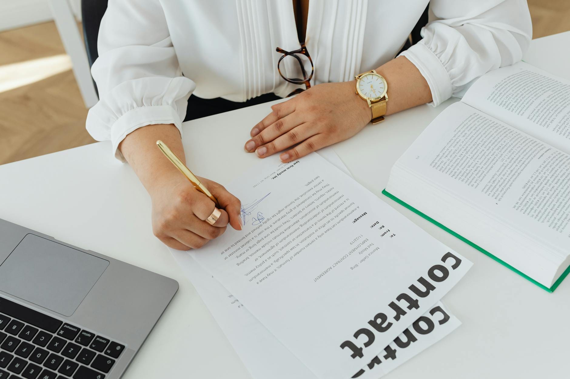 Bizneswoman podpisuje umowę przy biurku z laptopem i książką