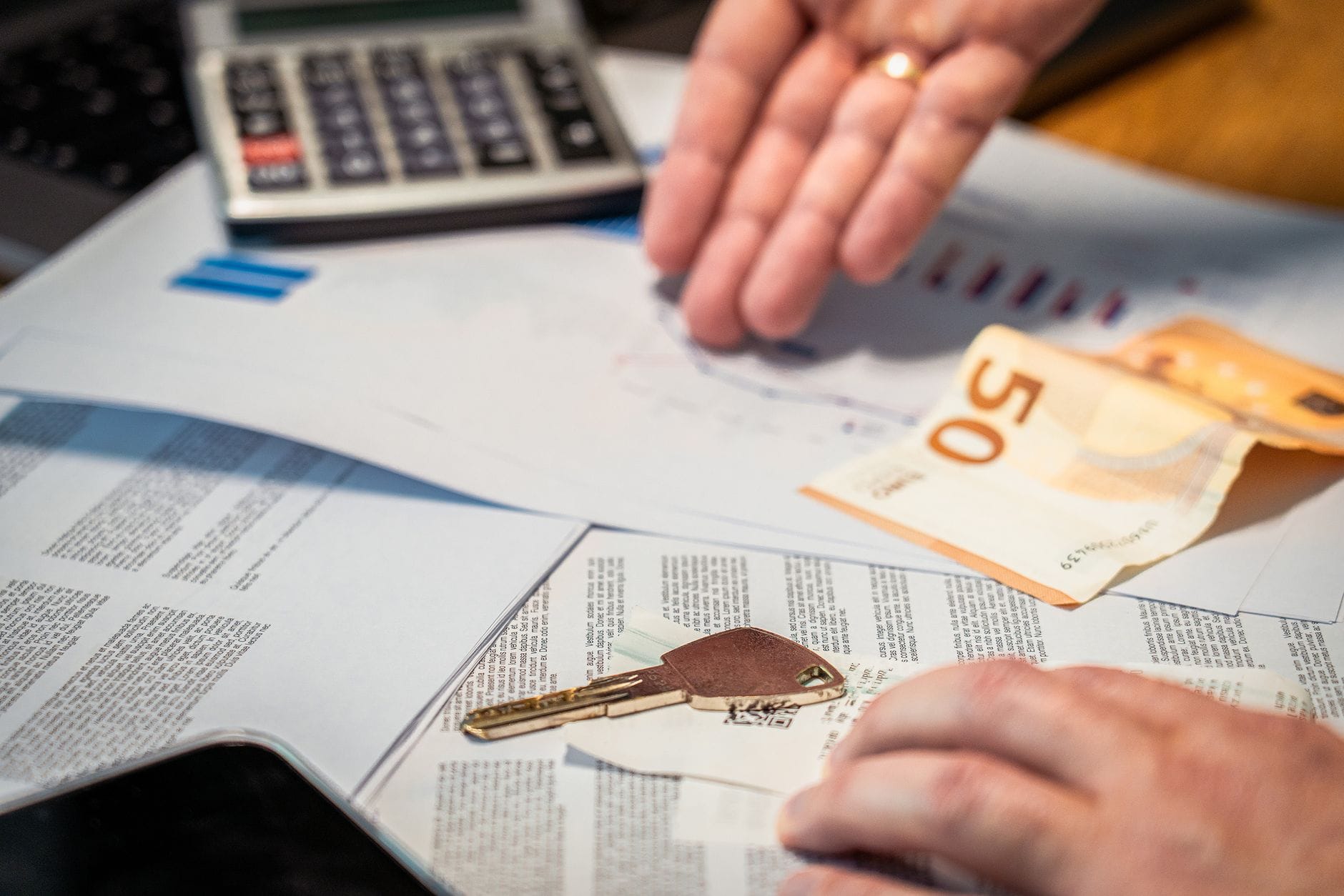 Dłonie nad dokumentami finansowymi z banknotem 50 euro i kluczem