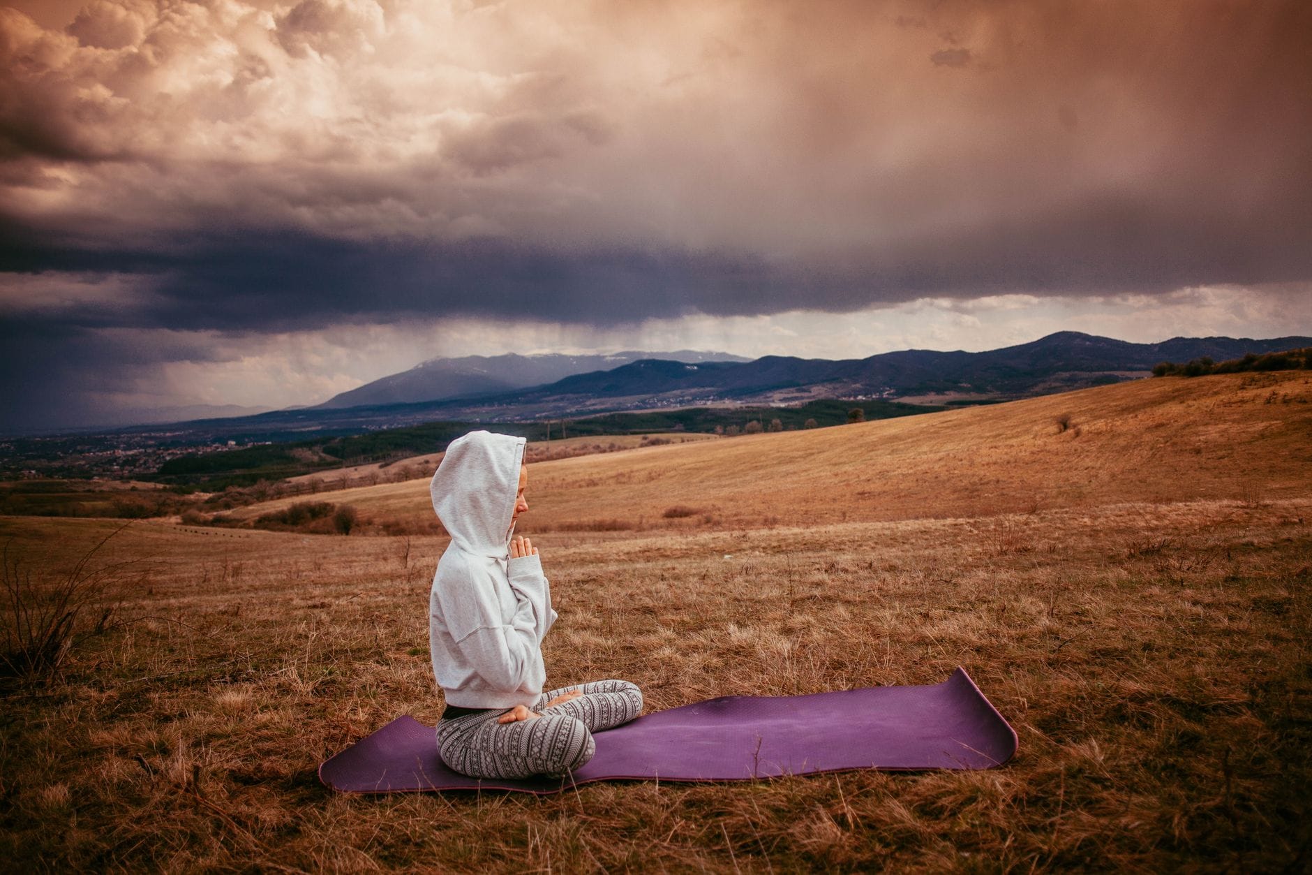 Rola medytacji w codziennej duchowości: jak praktyki kontemplacyjne kształtują religijne doświadczenie człowieka Kobieta medytująca na macie do jogi w spokojnym wiejskim krajobrazie