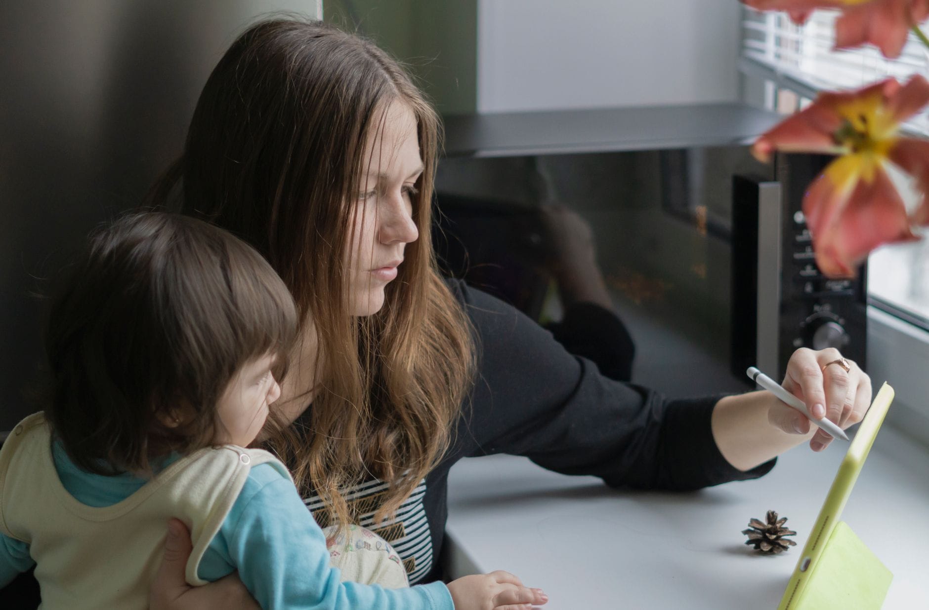 Mama pracuje na tablecie, trzymając na rękach małe dziecko